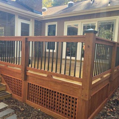 Wooden backyard deck with black railings and lattice skirting beside a house