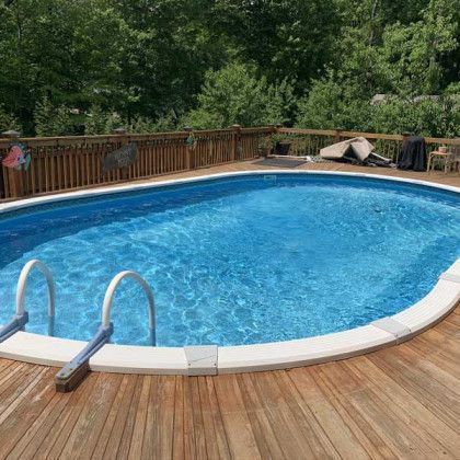 Backyard swimming pool with a wooden deck and ladder, bordered by a fence and trees.