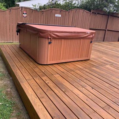 Covered hot tub on a wooden deck in a fenced backyard.