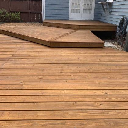 Wooden deck with a raised platform and walkway beside a blue house in a backyard