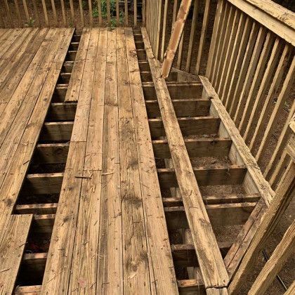 Weathered wooden planks covering a porch floor beside exposed joists and railings under construction