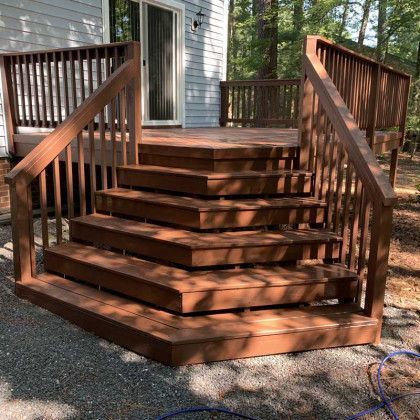 Wooden outdoor deck with curved front steps and railings beside a house, in a wooded yard.