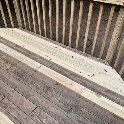 Weathered wooden deck corner with vertical railings and dirt ground beyond.