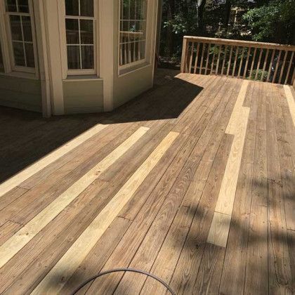 Wooden deck with sunlit and shaded planks beside a house and railing.