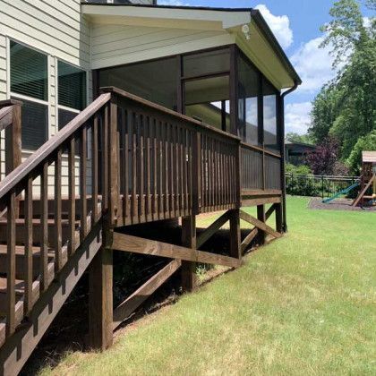 Wooden porch deck with stairs beside a house, overlooking a green backyard.