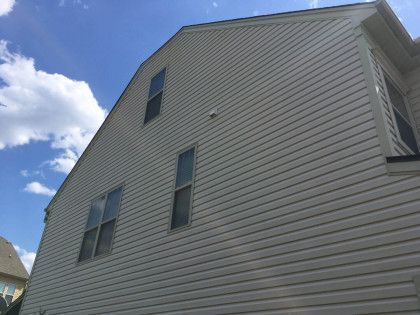 Side of a beige house with gray siding and several windows against a blue sky