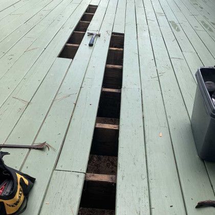 Open floorboards on a pale green deck, exposing a long gap down the center.