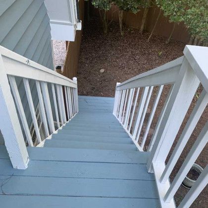 Looking down a light blue wooden staircase with white railings to a small fenced yard below