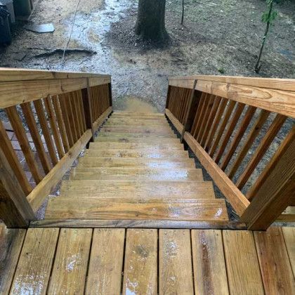 Wet wooden stairs descending to a muddy yard with a large tree