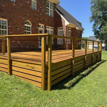 Wooden deck with railings beside a red brick house on a sunny lawn