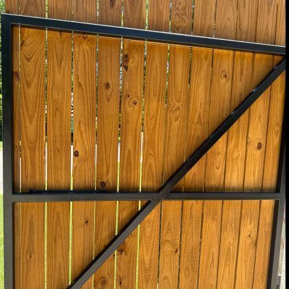 Wooden gate with black metal frame and diagonal brace against a wood fence