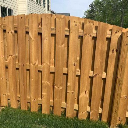 Wooden privacy fence with vertical slats and a curved top in a grassy backyard area