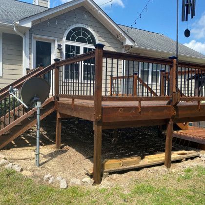 Wooden backyard deck with stairs and railing attached to a house, with a satellite dish in the foreground