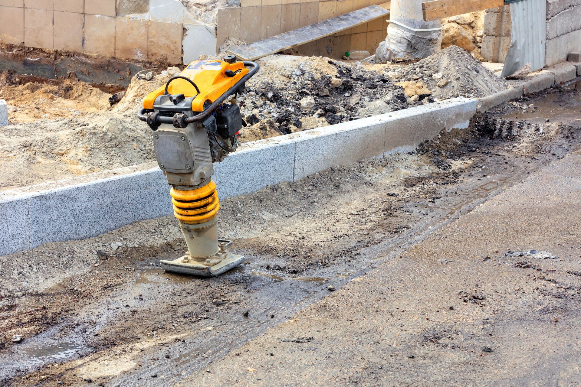 Un martillo neumático amarillo rompe el hormigón junto a un bordillo en una obra en construcción.
