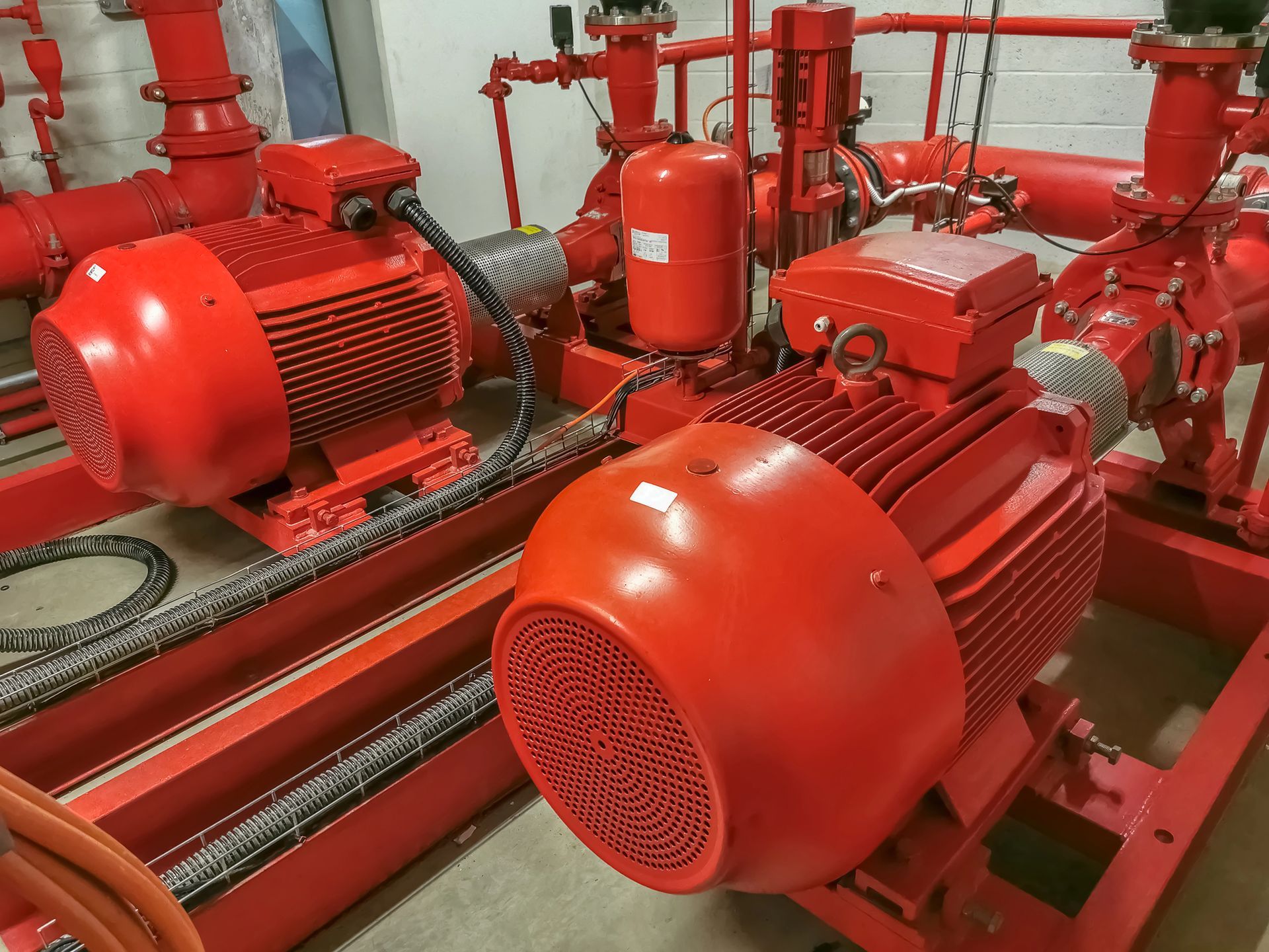 Bombas y motores industriales contra incendios de color rojo en una sala de máquinas, pintada de rojo brillante con tuberías y manómetros.