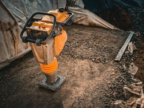 Un compactador amarillo compacta la tierra en una obra de construcción, con lonas y grava cerca.