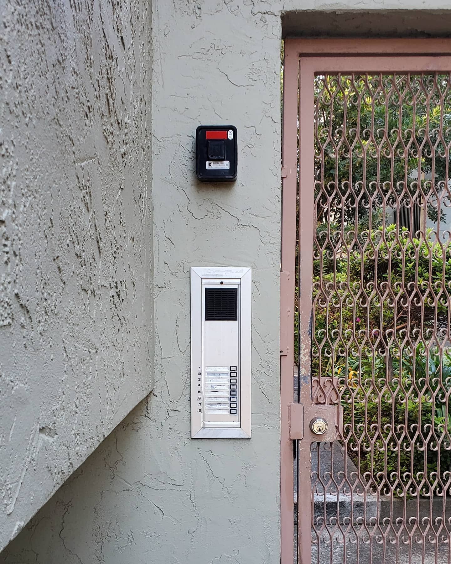 An intercom system and security camera mounted on a textured wall next to a metal gate.