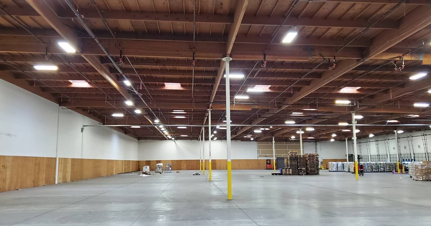 Empty warehouse with concrete floor, wooden beams, bright lights.