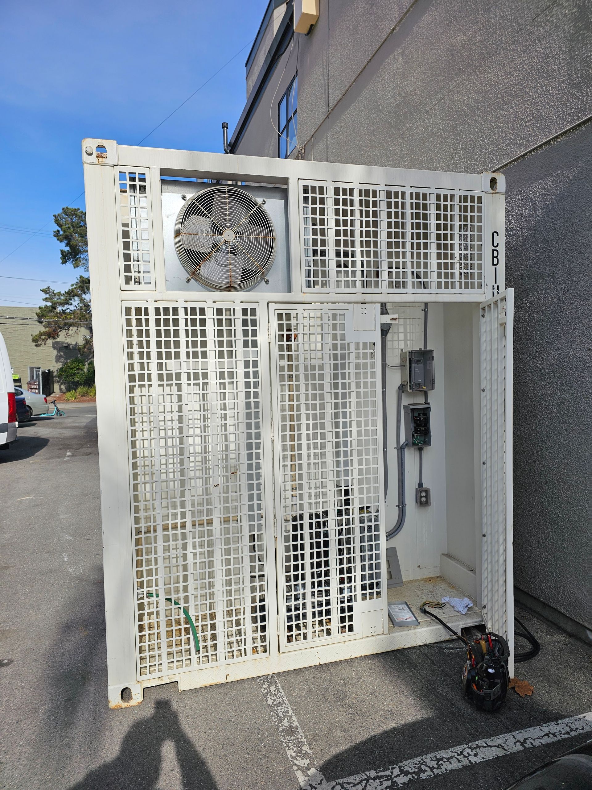White industrial cooling unit with fan and caged exterior against a gray building.