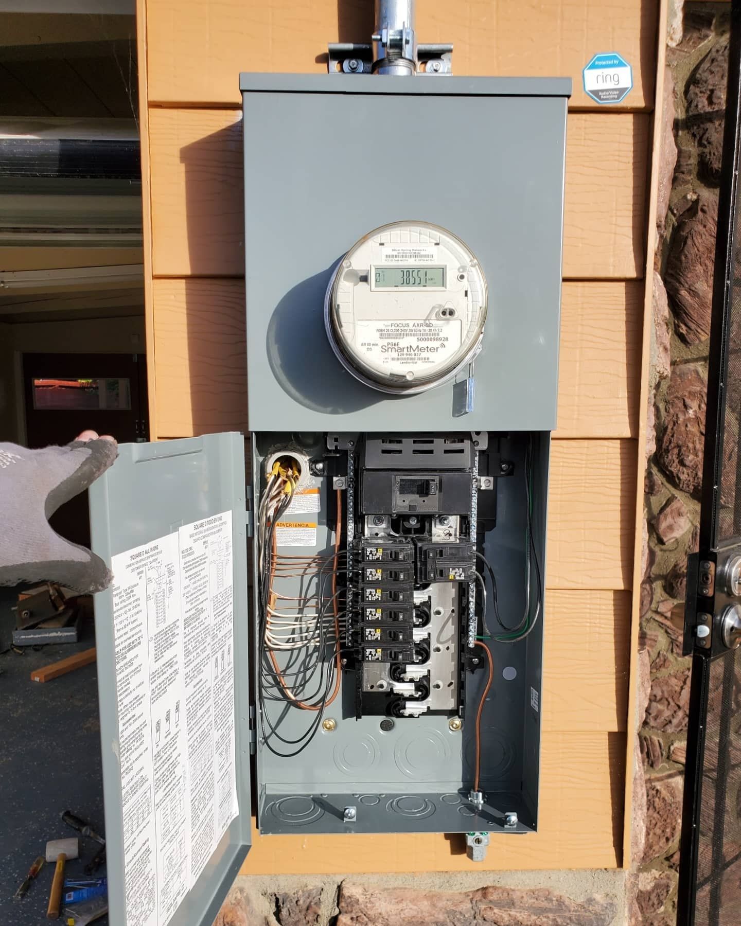 Exterior electrical panel mounted on a beige building with open panel door showing breakers and wiring.