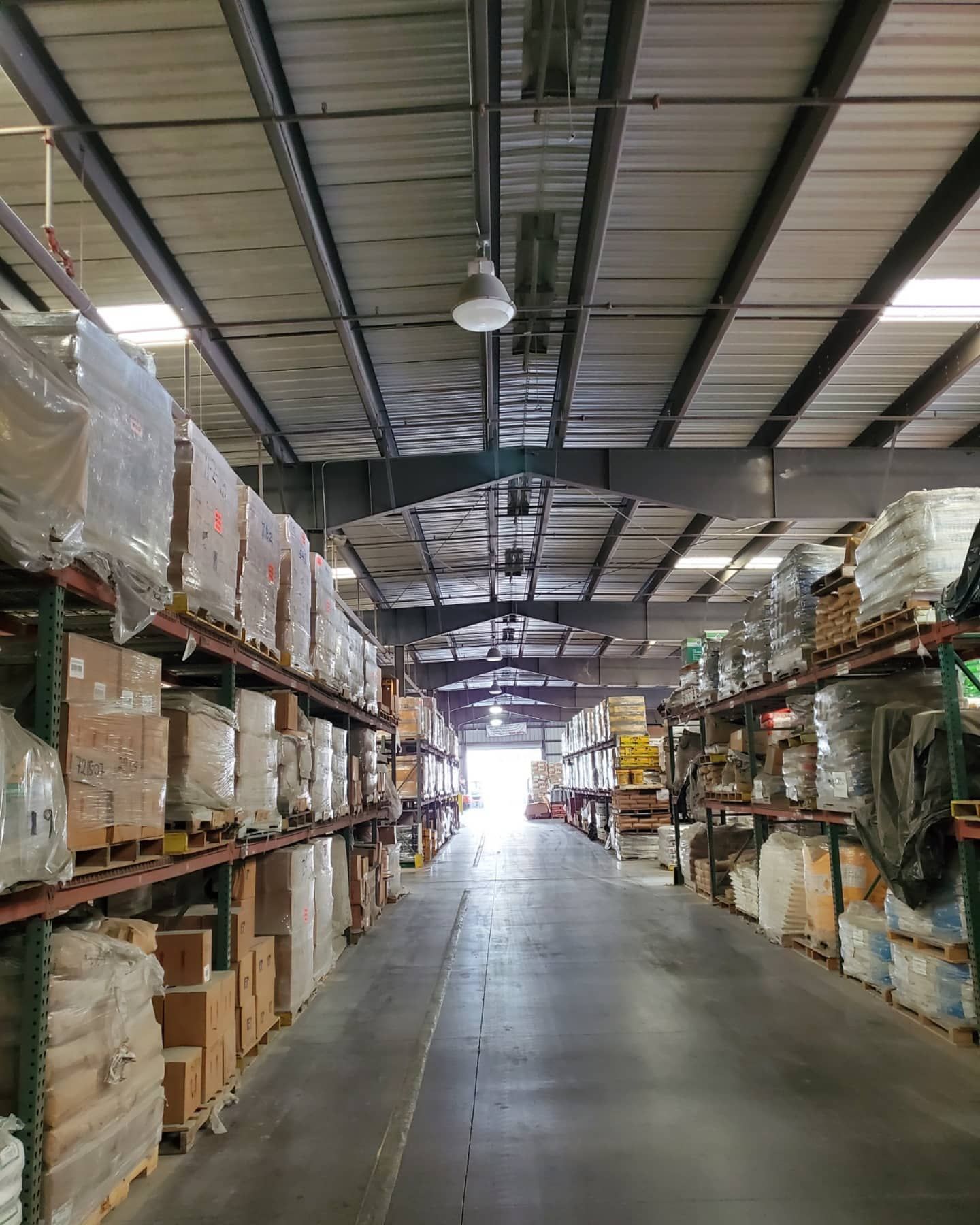 Warehouse interior with rows of packed shelves and bright light at the end of the aisle.