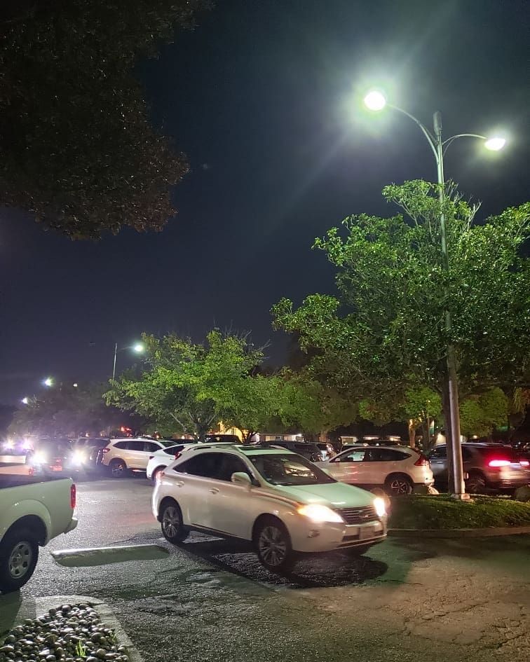 Nighttime parking lot with cars, trees, and streetlights illuminating the scene.