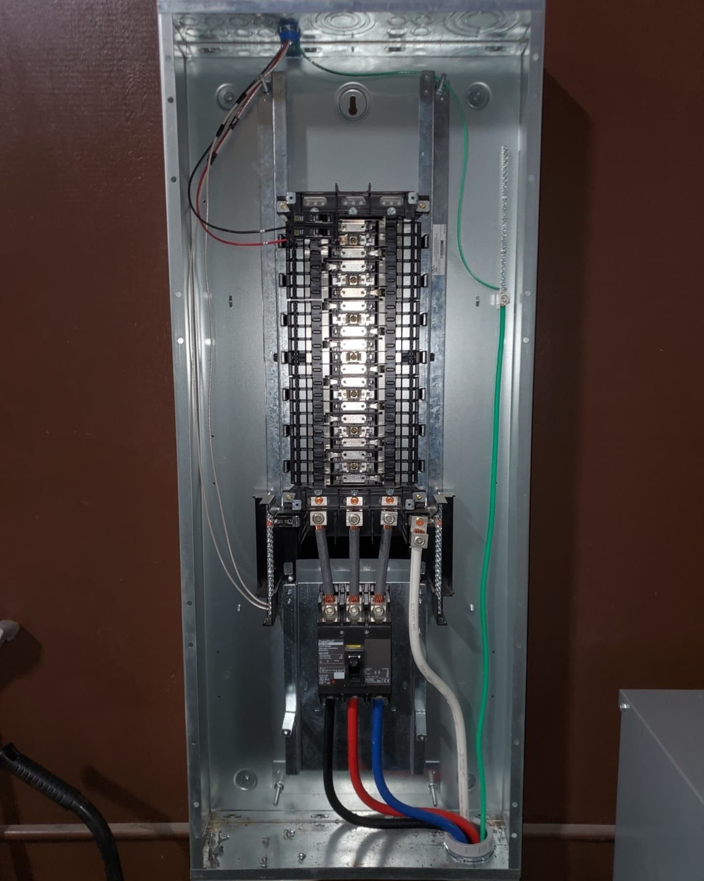 Open electrical panel with wires connected. Brown, blue, and black wires are visible. Metallic enclosure.