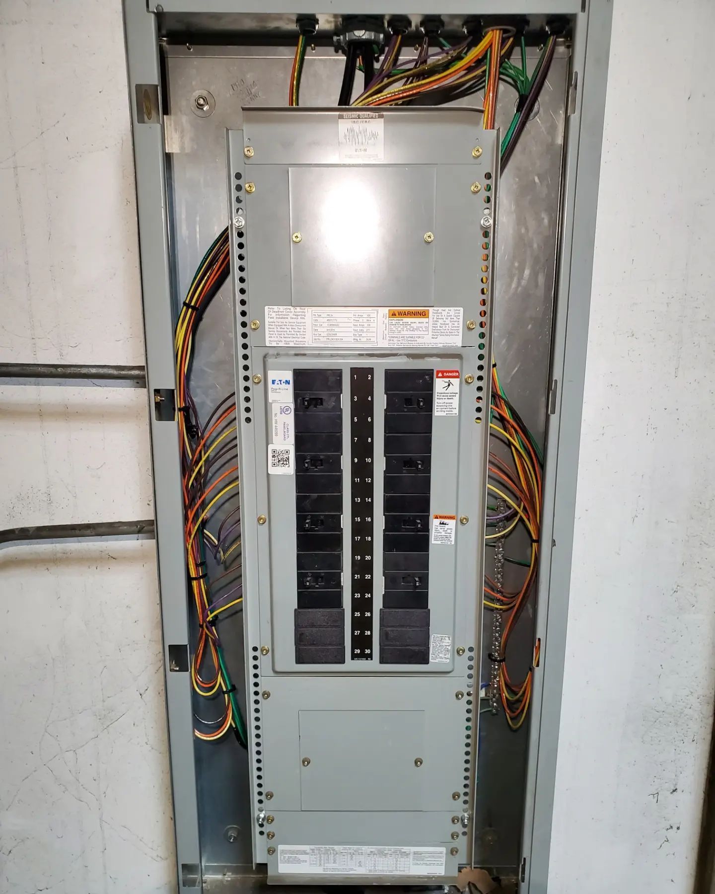 Electrical panel in a recessed metal enclosure, surrounded by colored wires. Grey with black breakers.