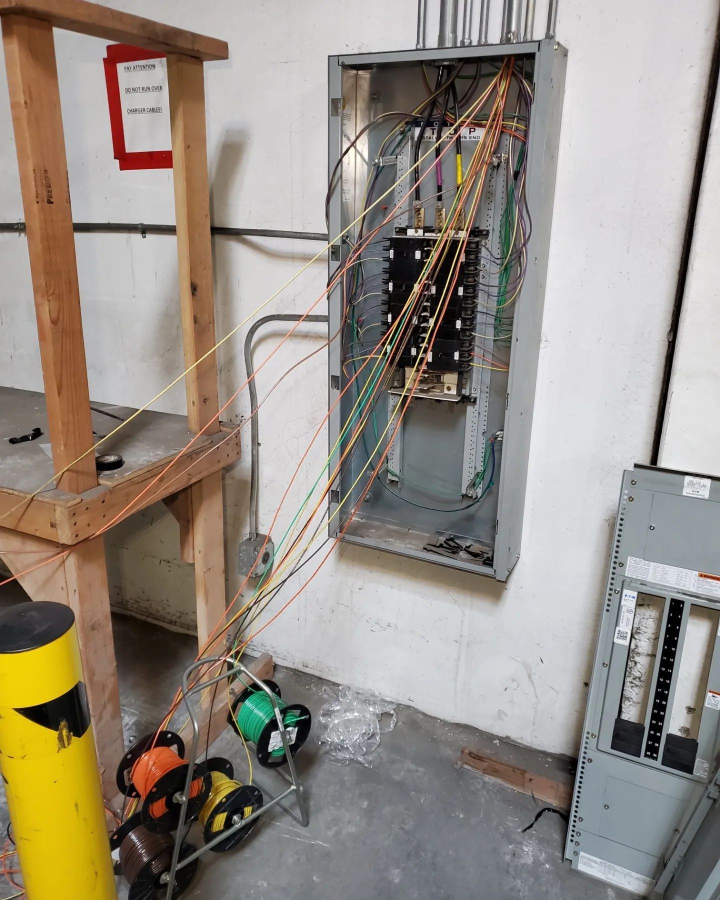 Open electrical panel with exposed wires; spools of colored wire nearby.