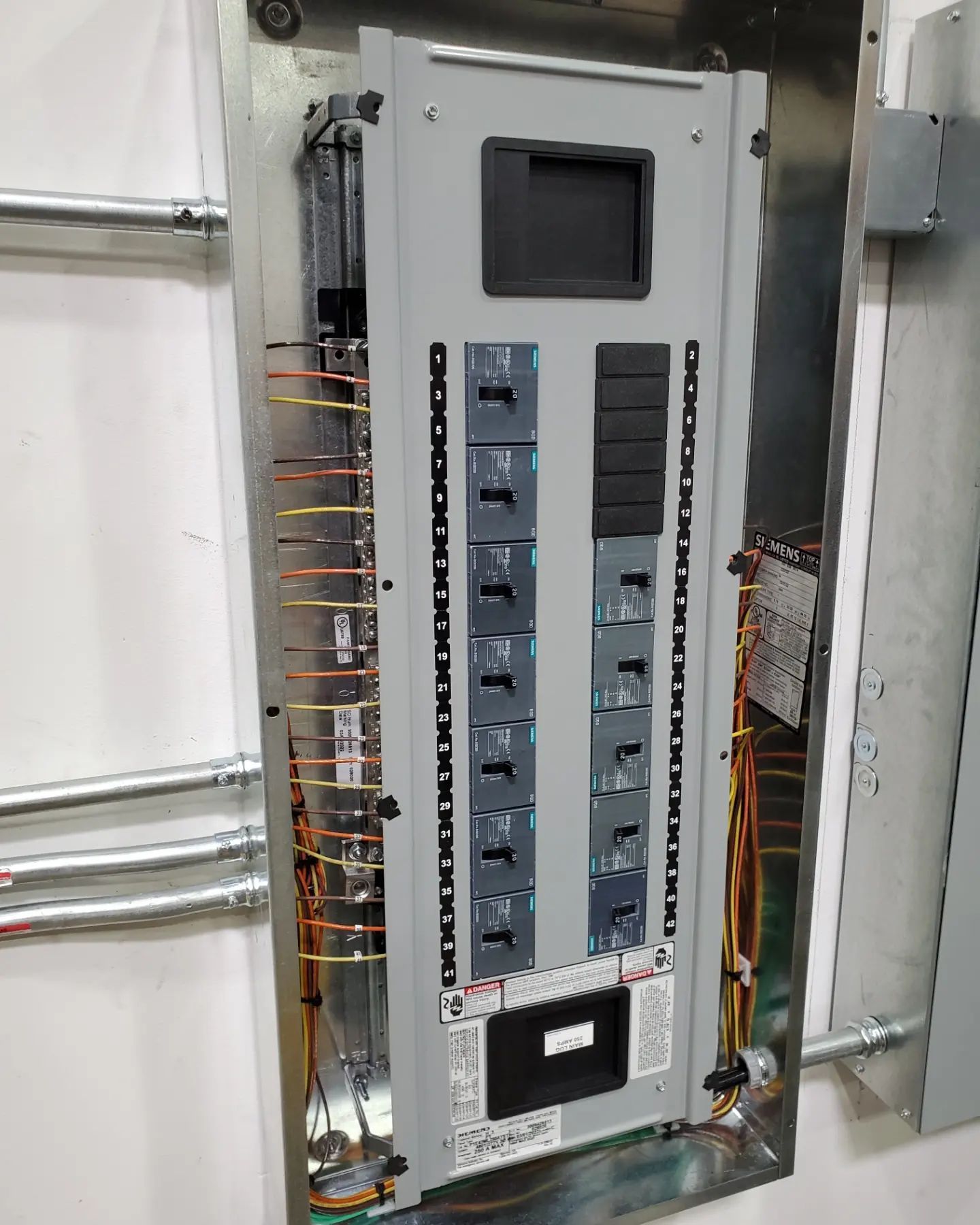 Electrical panel with circuit breakers and wiring inside a metal box on a wall.