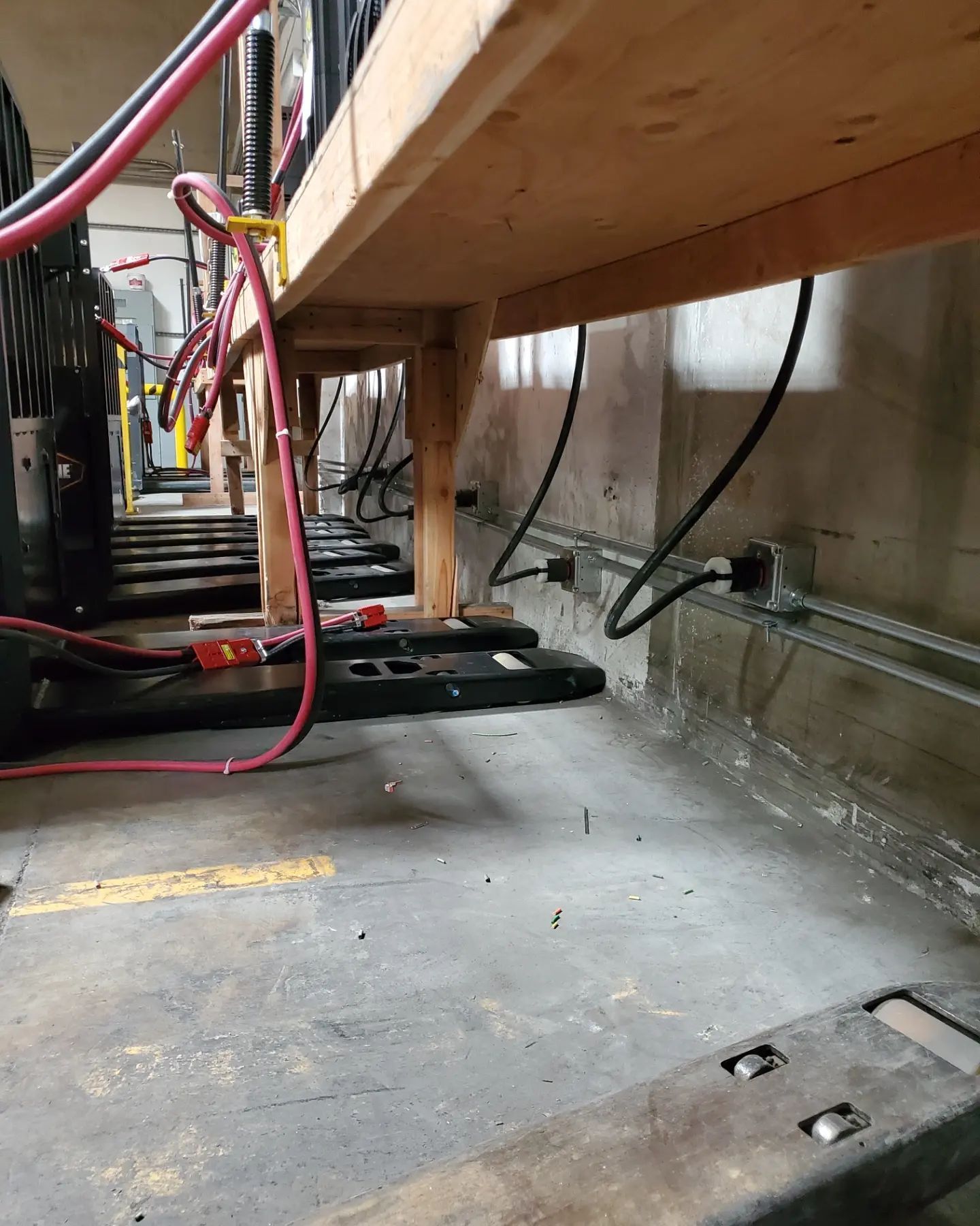 Row of electrical equipment under a wooden shelf, with wiring and cables, inside a utility room.
