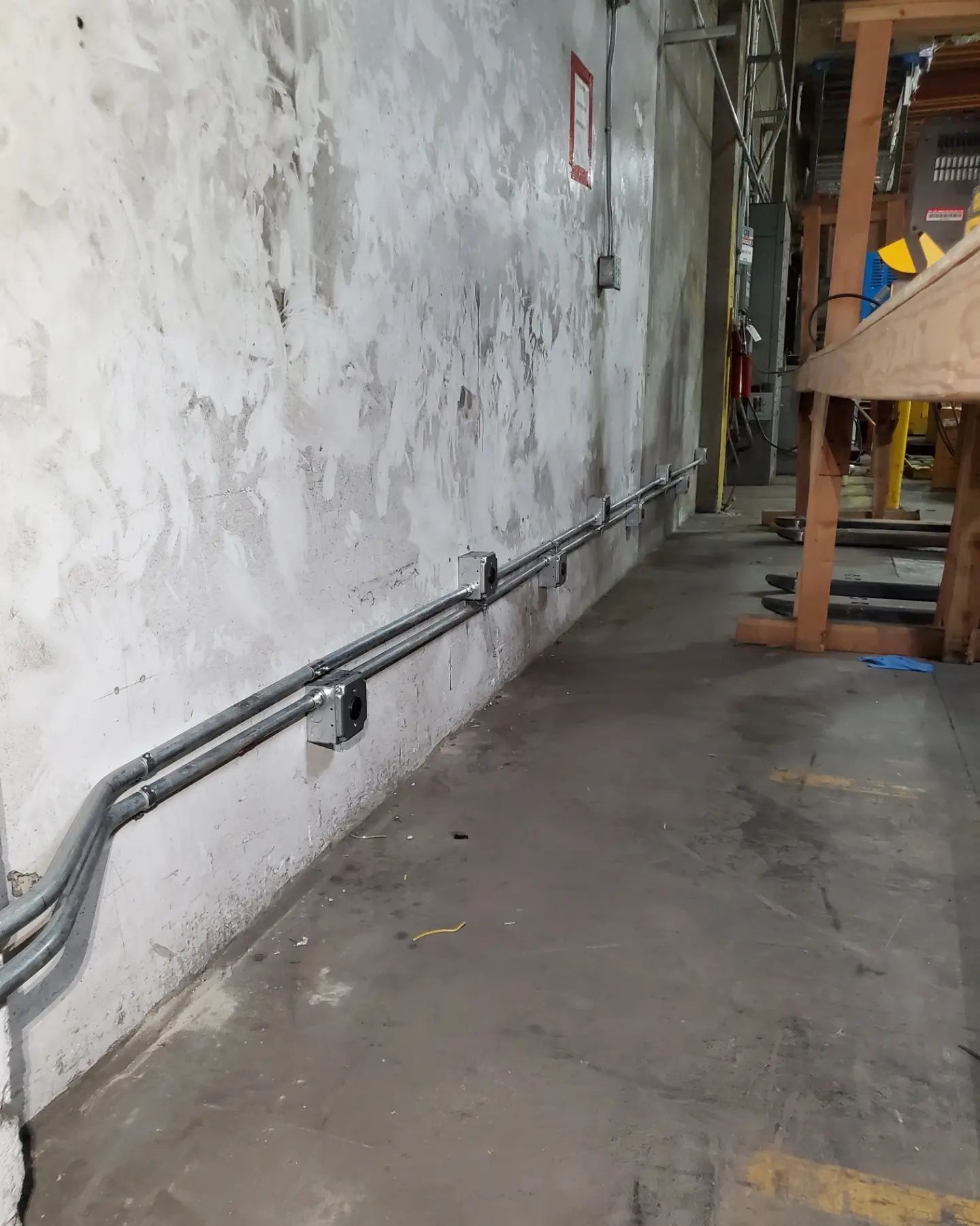 Gray electrical conduit runs along a textured, aged concrete wall in a factory.