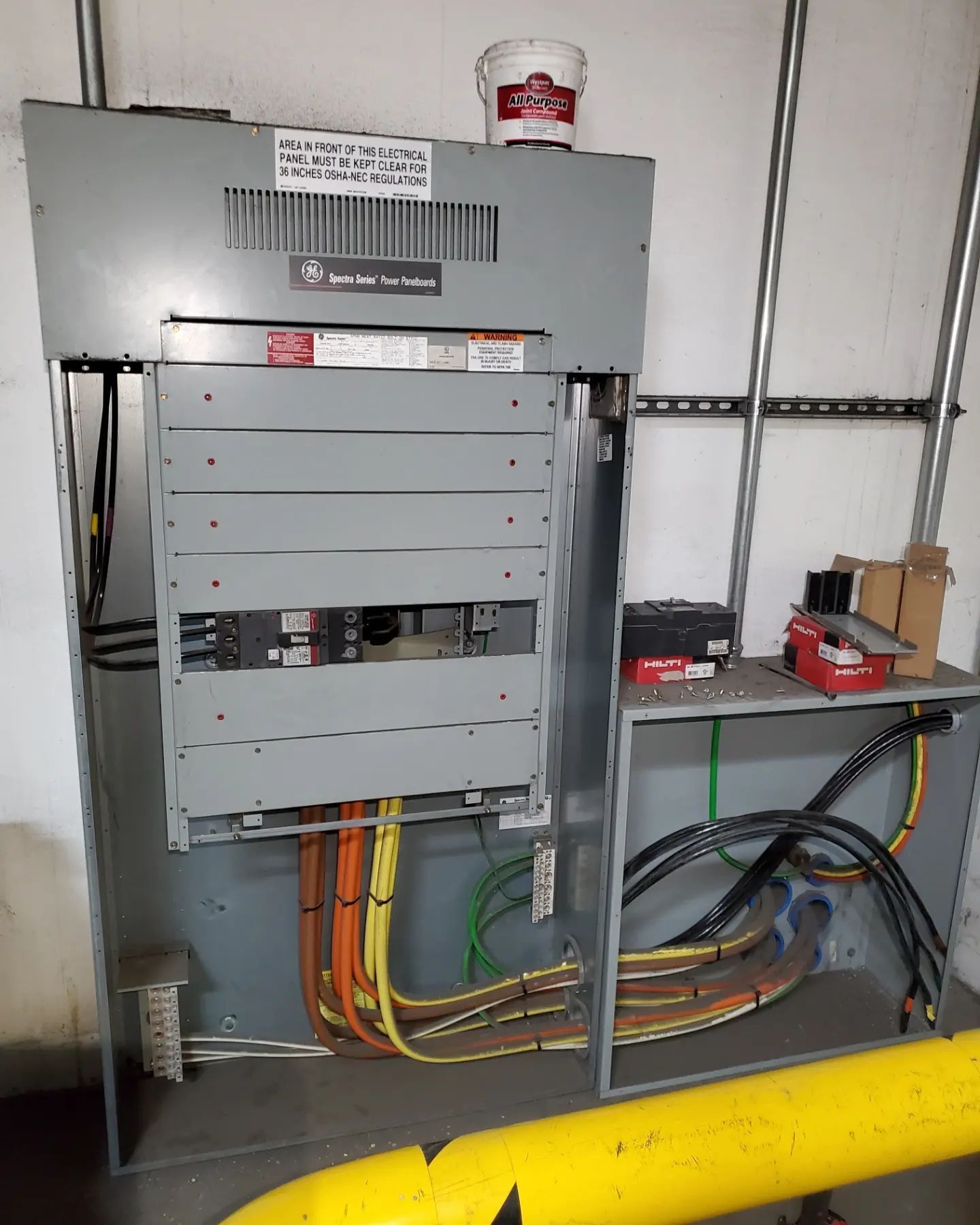 Electrical panel with open door, showing wires and breakers. Yellow and black conduits are visible.
