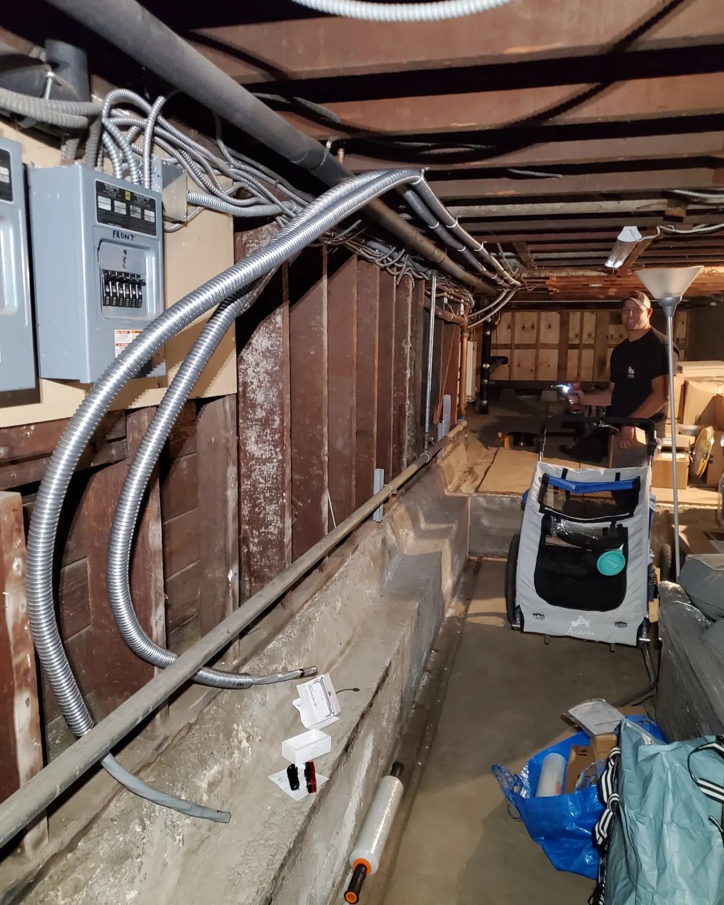 Electrical work in a basement: conduit wiring along wooden beam; person inspecting, electrical panels in view.