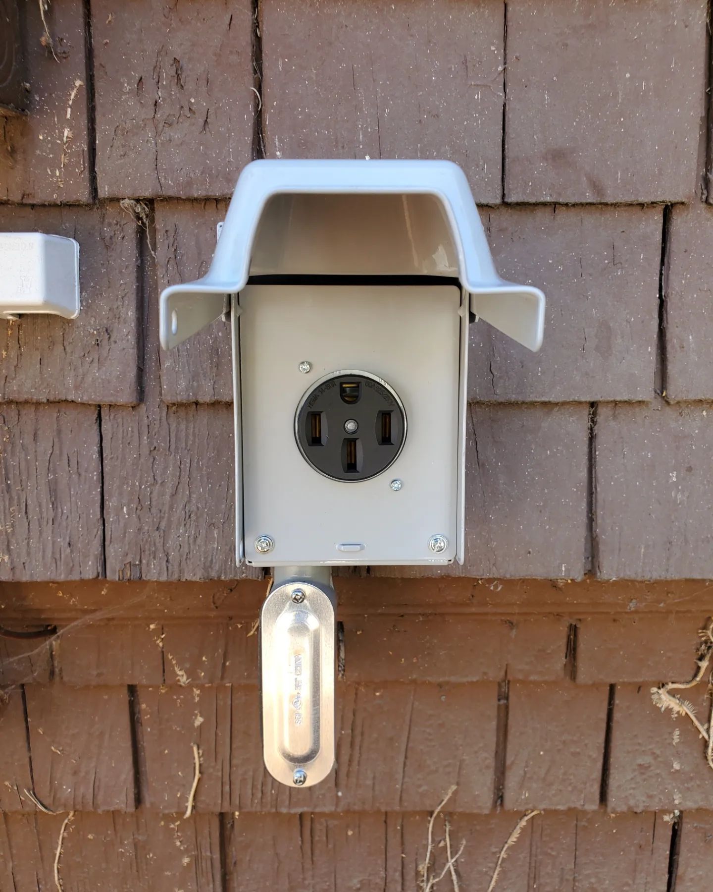 Gray electrical outlet with cover on brown siding.