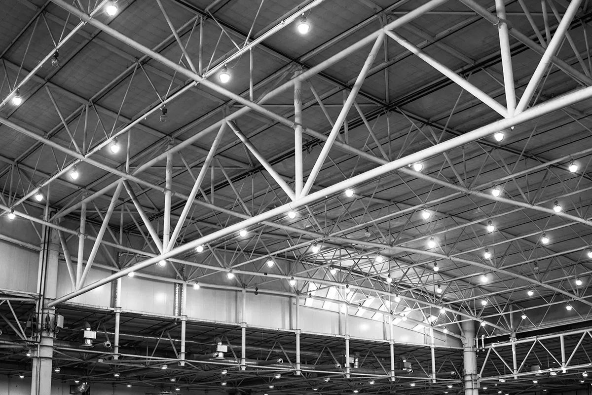 Steel truss roof structure with overhead lighting in a large interior space.