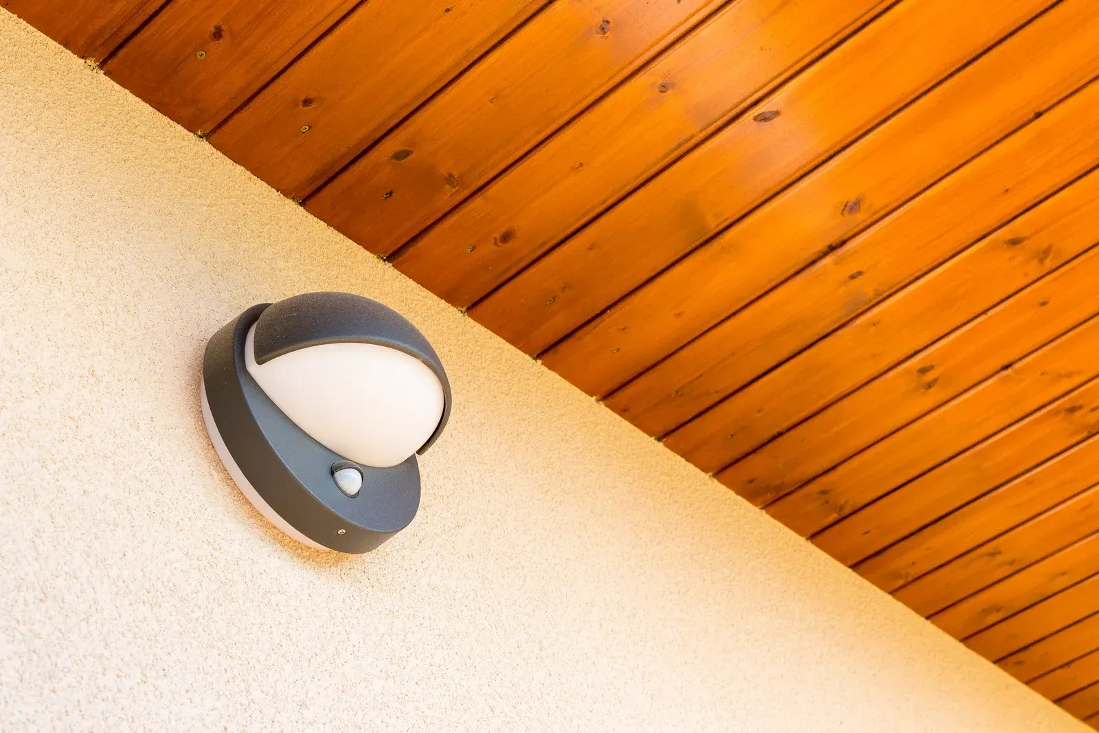 Outdoor light fixture on a textured beige wall under a wooden slatted ceiling.