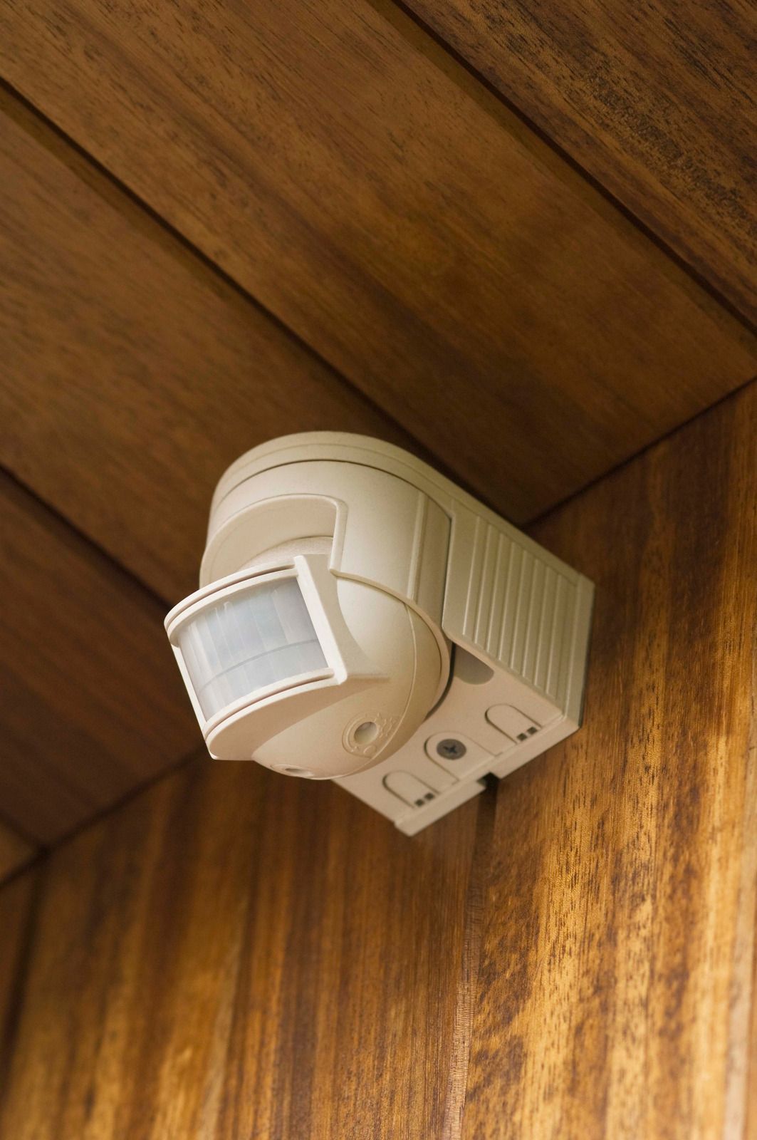 Motion sensor light mounted on wooden wall. White device angled towards the viewer.