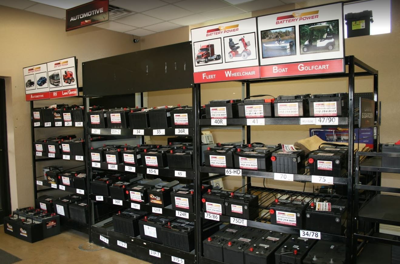 Batteries displayed on shelves in a retail store. Product signs, dark metal shelving, tan walls.