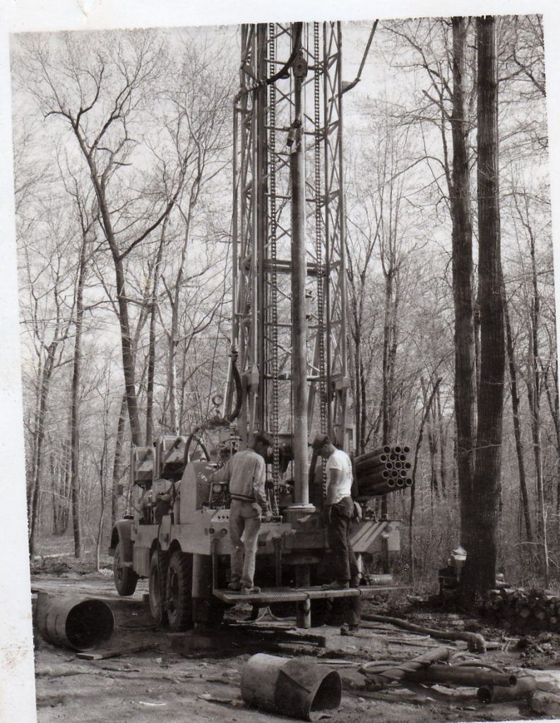 A black and white photo of a drilling rig in the woods