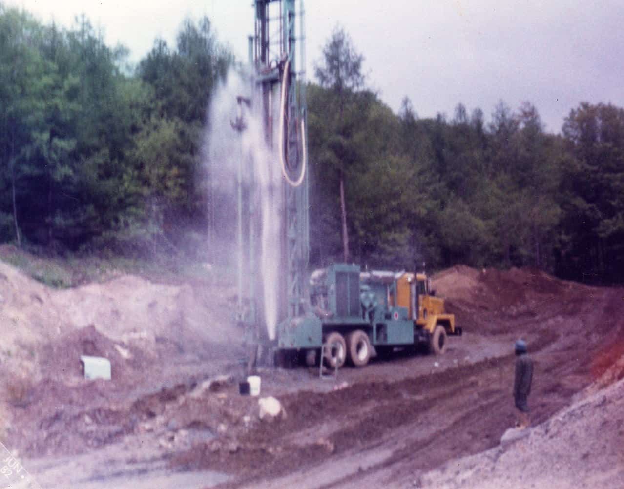 A truck is drilling a hole in the ground in a dirt field.