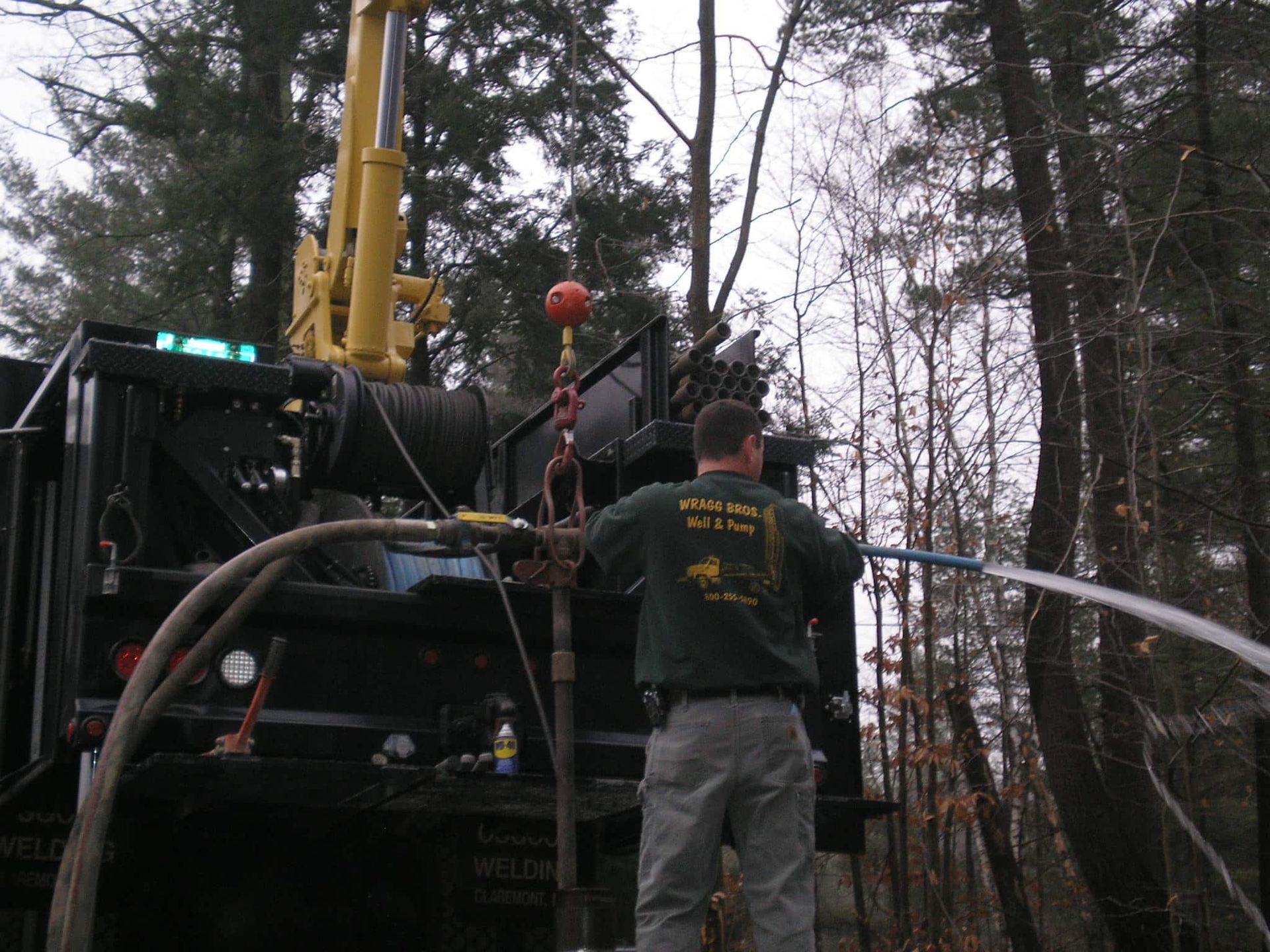 A man is standing in front of a machine that has a hose attached to it from Wragg Brothers Well Drilling