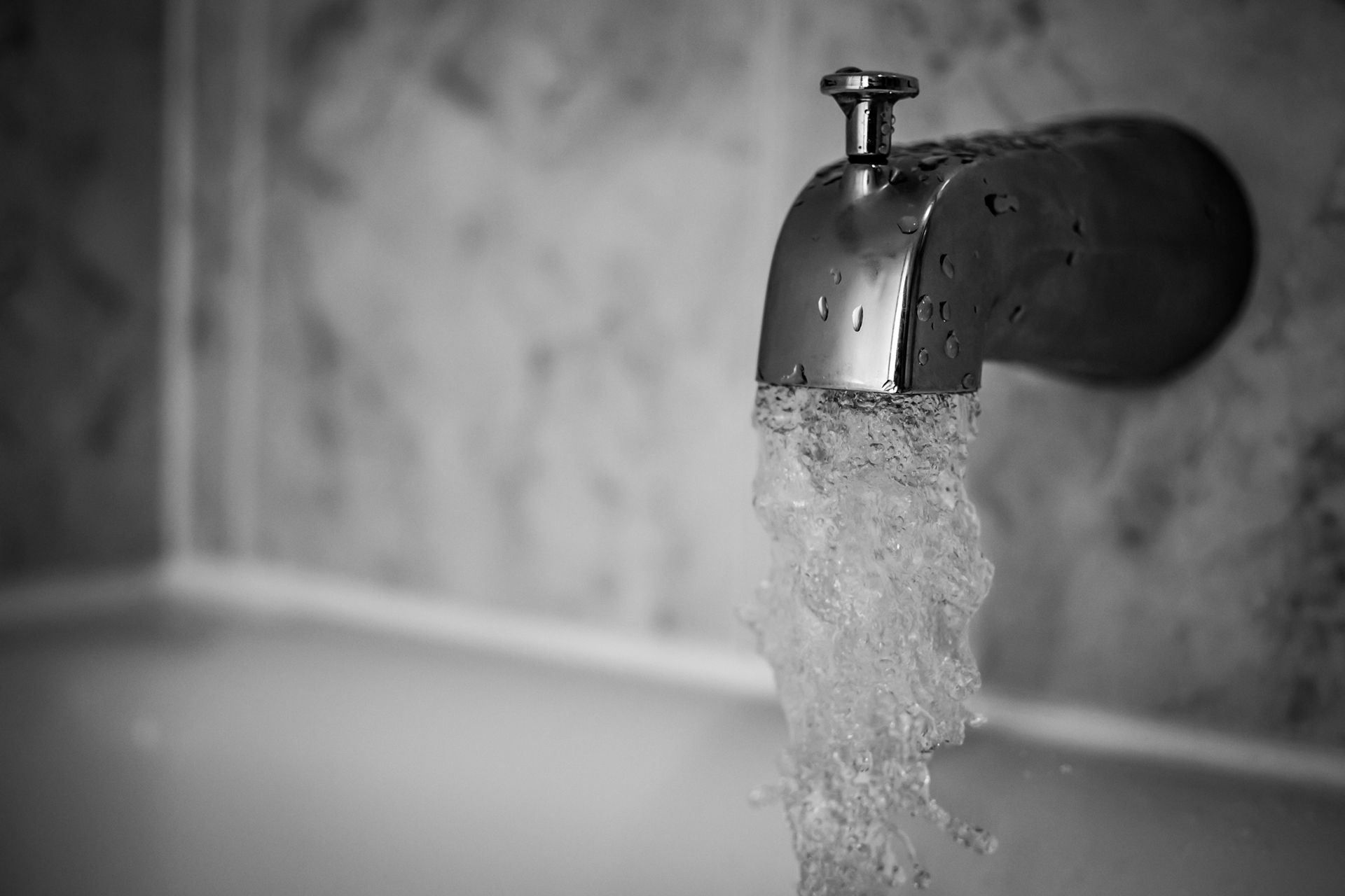 Black-and-white close-up of a running bathtub faucet pouring water into a sink or tub
