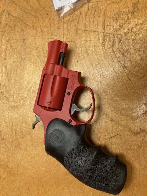 Red and black revolver with a black grip resting on a wooden surface