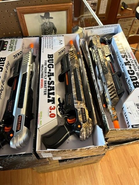 Boxes of model toy guns and accessories on a table, including several black and orange rifles.