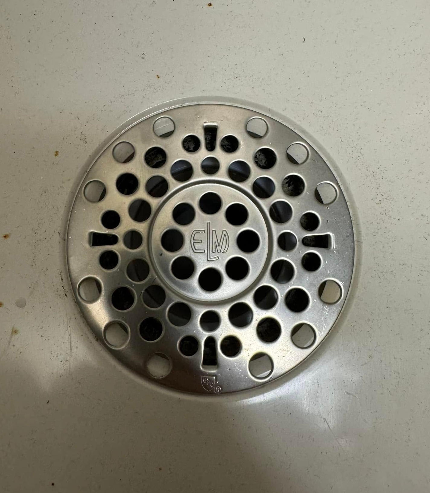 Round metal floor drain cover with perforated holes on a light-colored floor.