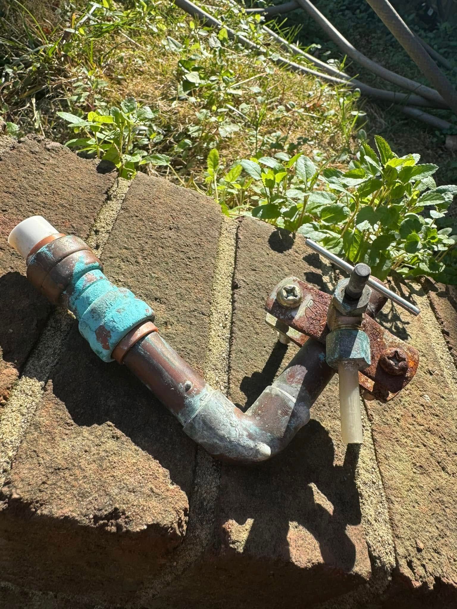 Old metal pipe and shutoff valve with rust, mounted on a concrete block outdoors in sunlight