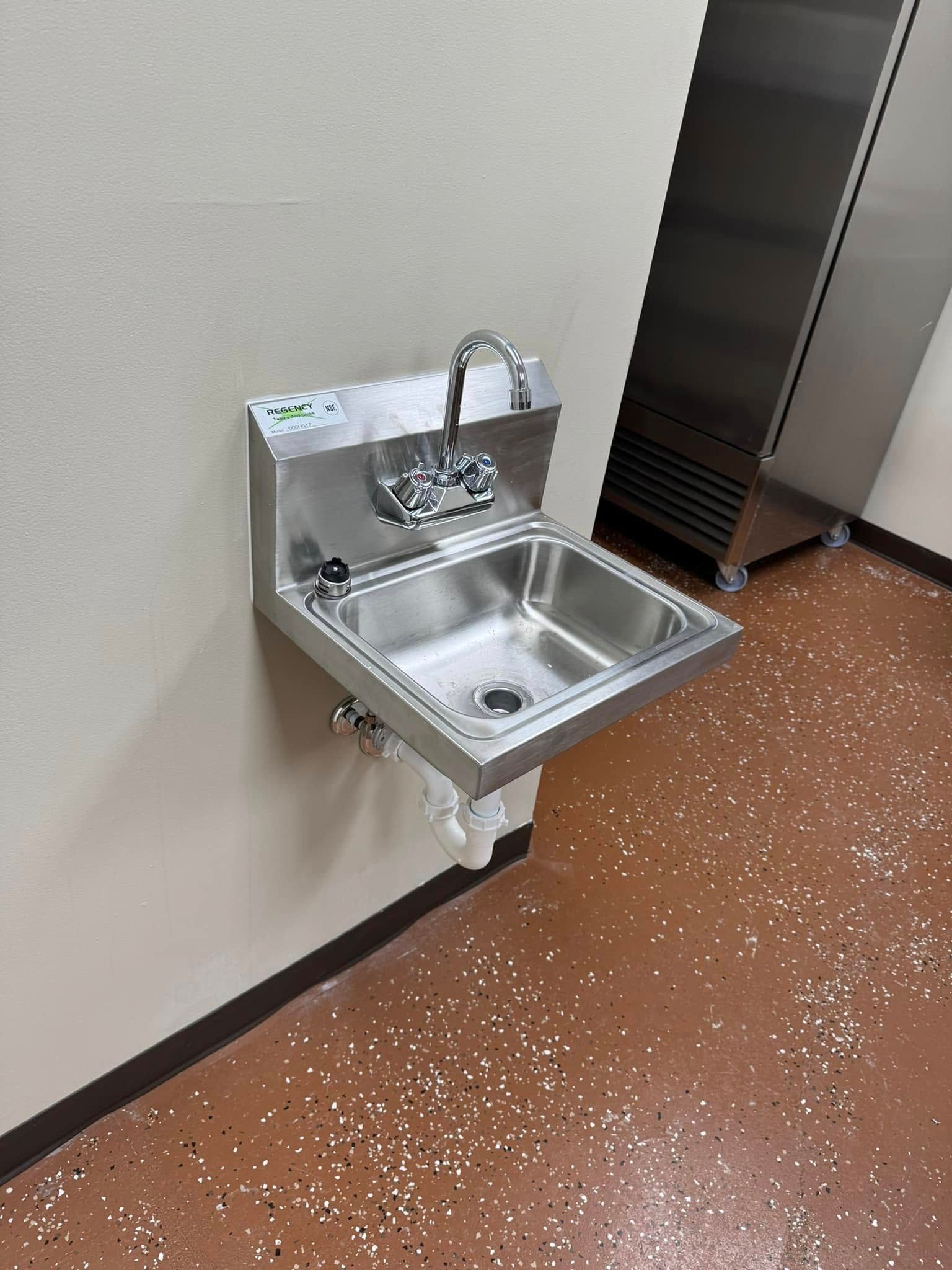 Small stainless steel wall-mounted sink with faucet in a hallway by a door.
