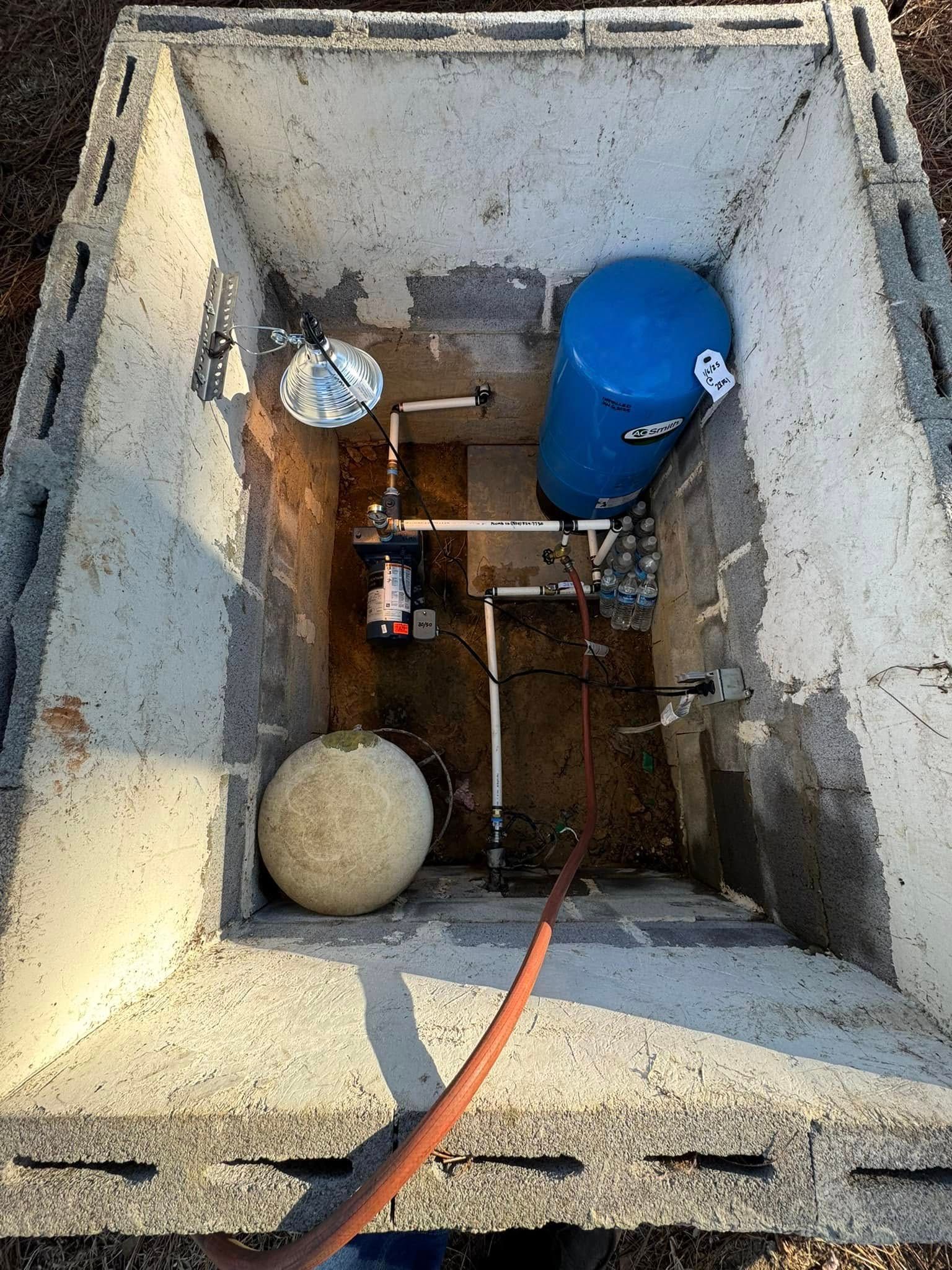 Top-down view of a concrete utility pit with pipes, a blue tank, and a small spherical float.