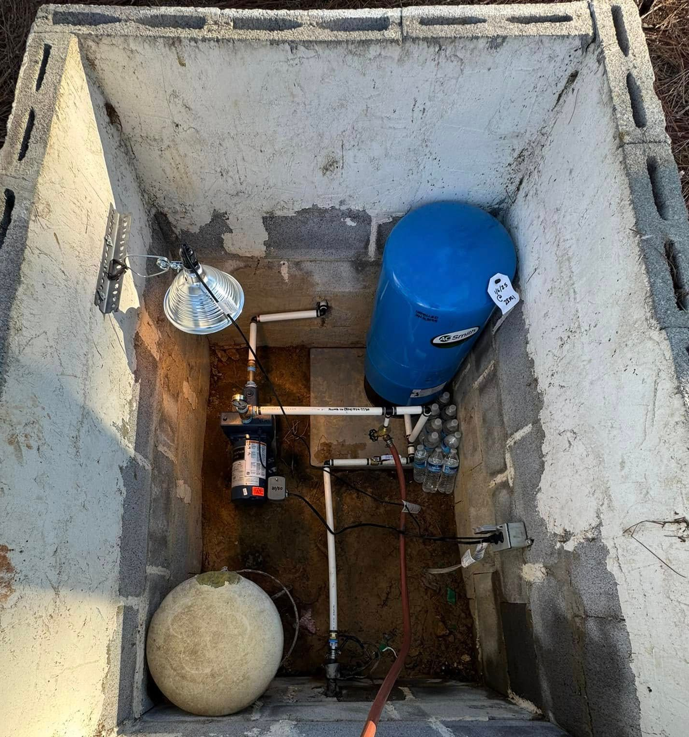 Overhead view of a utility pit with pipes, valves, a blue tank, and a round float on the floor